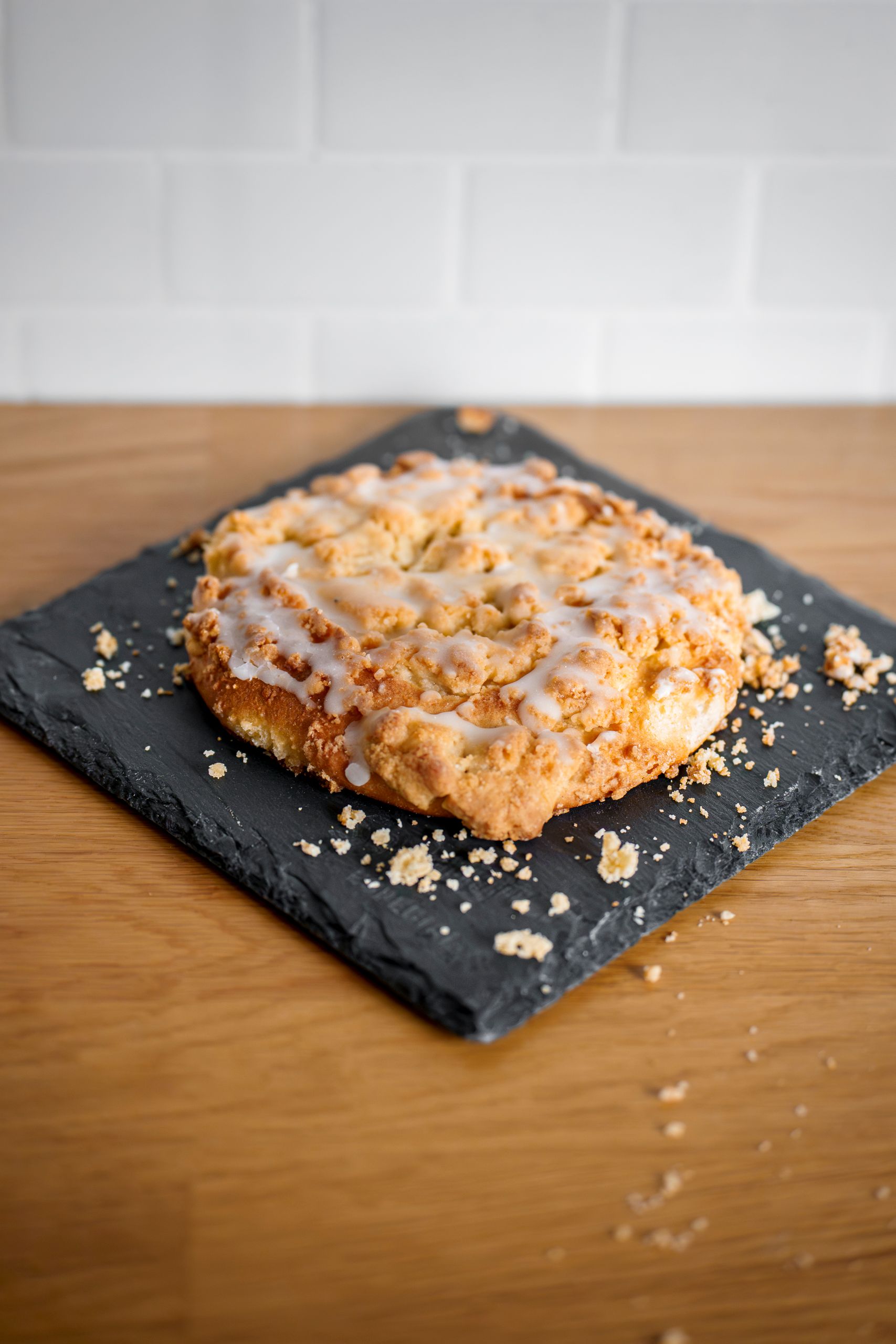 Appetizing crumb cake topped with icing served on a slate with wooden background.