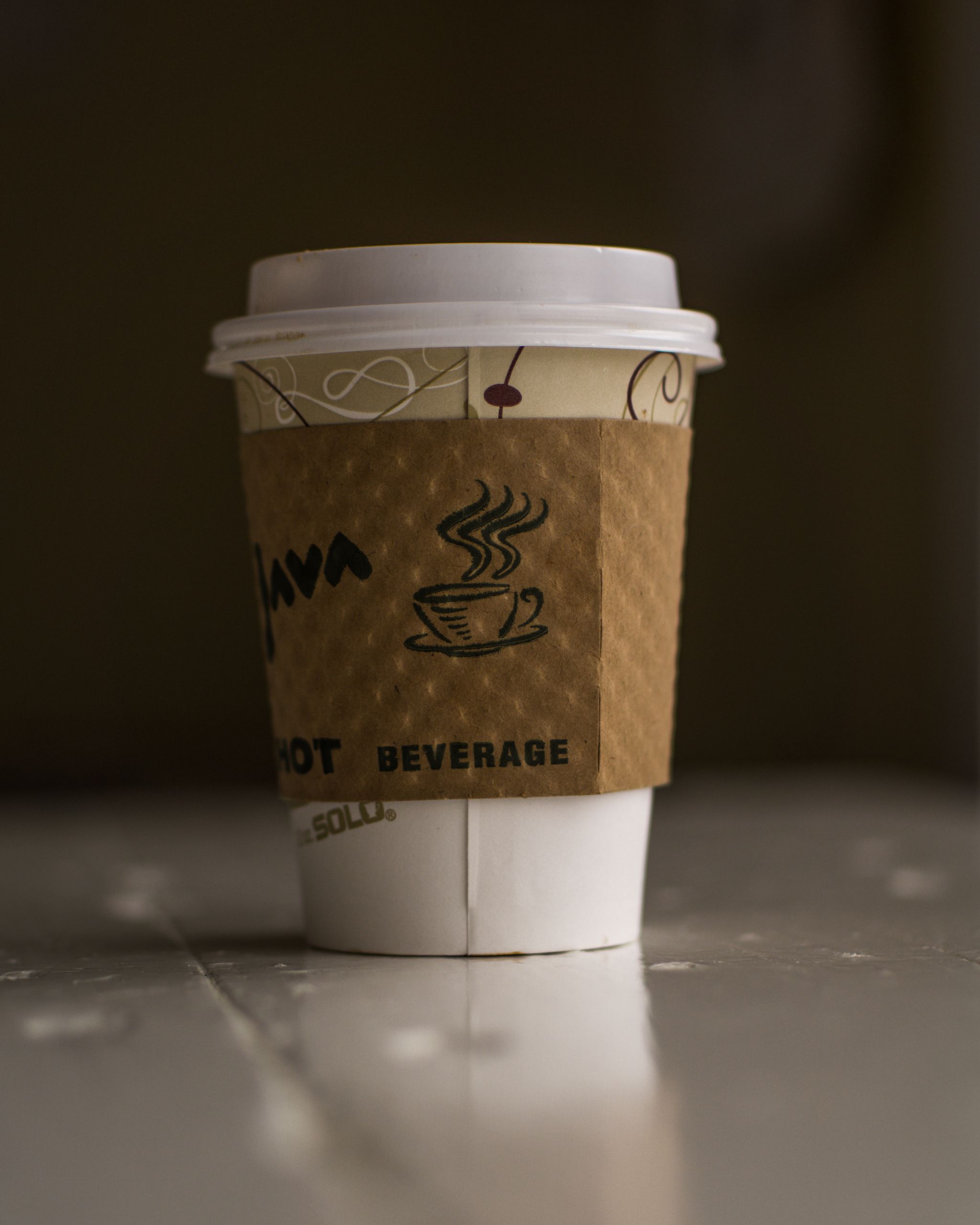 Close-up of a disposable coffee cup with a sleeve, on a table, emphasizing the warm beverage.